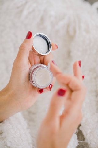 hands-with-red-nails-hold-a-small-cosmetics-container - LeCil